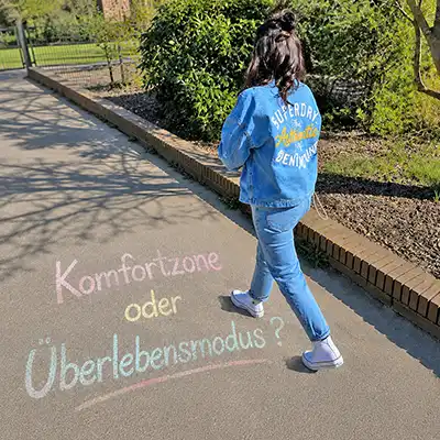 Frau auf einem Weg mit Kreideschrift „Komfortzone oder Überlebensmodus?“ auf dem Boden – Symbolbild für Selbstreflexion, persönliche Entwicklung und innere Heilung.